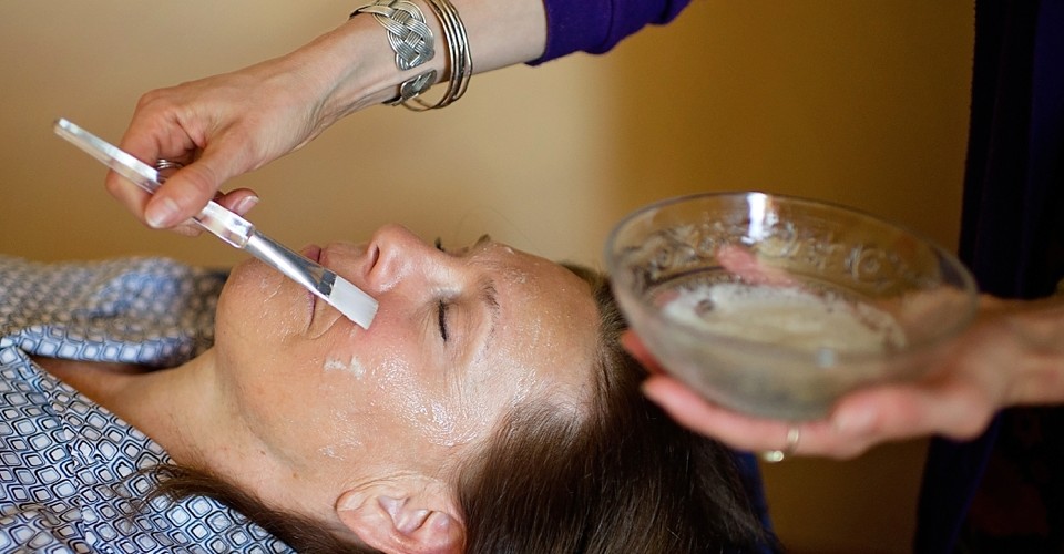 Woman receiving a facial treatment with a brush and cream.