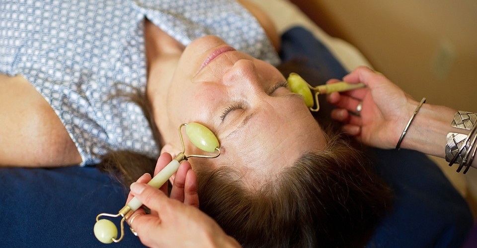 Woman receiving a relaxing facial massage with jade rollers.