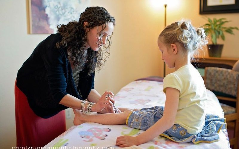 A woman painting a young girl's nails in a cozy room.