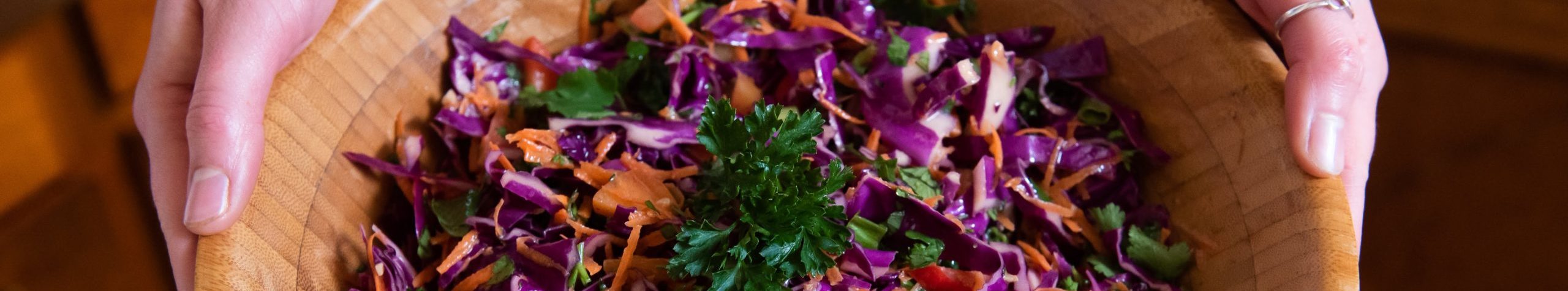 Colorful coleslaw with purple cabbage and fresh herbs in a wooden bowl.
