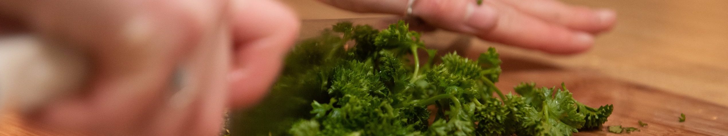 Hands chopping fresh green herbs on a wooden surface.